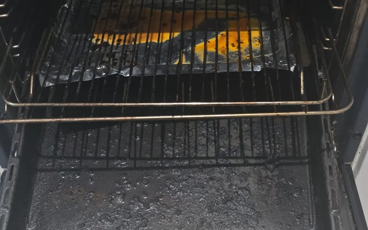 An oven before the clean, with baked-on dirt on the base and the door glass